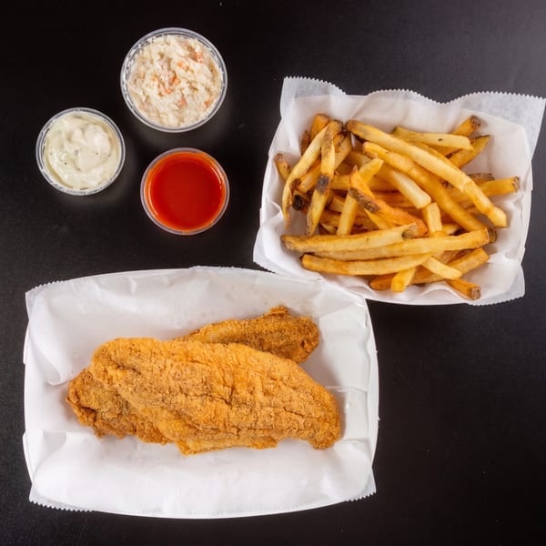 Fried fish fillets, french fries, coleslaw, tartar sauce, and hot sauce on a black surface.