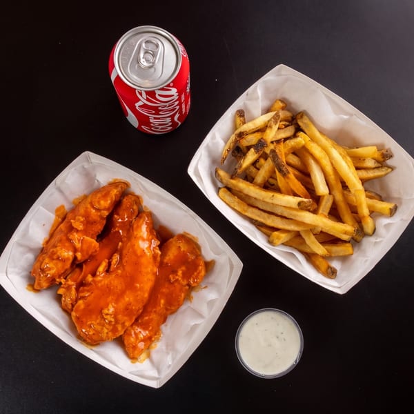 Top-down view of buffalo chicken tenders, fries, a Coca-Cola can, and ranch dressing on a black surface.