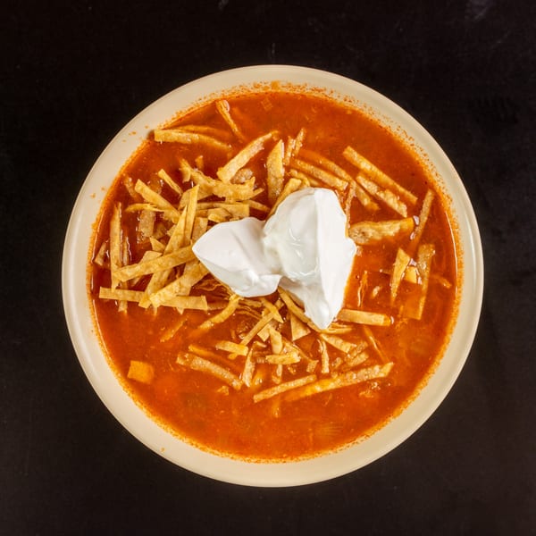 Overhead view of a bowl of red tortilla soup topped with crispy tortilla strips and sour cream.