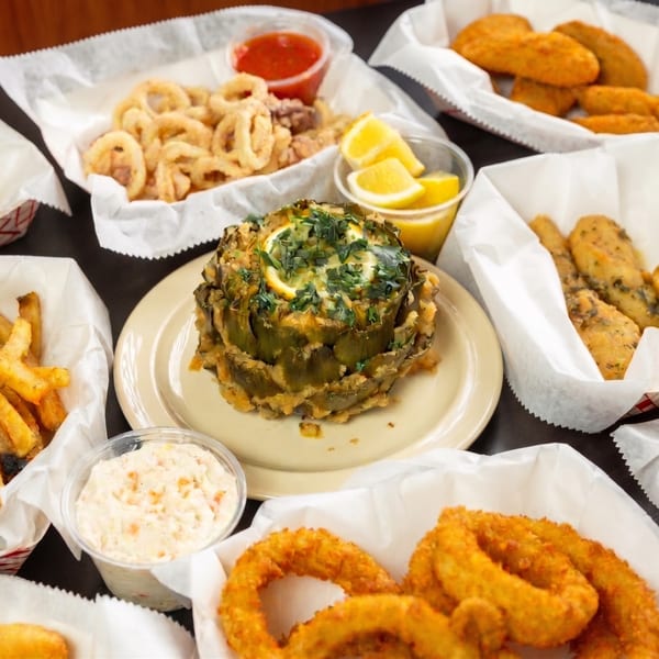 A table laden with fried seafood, including calamari, fish, onion rings, fries, and a stuffed artichoke.