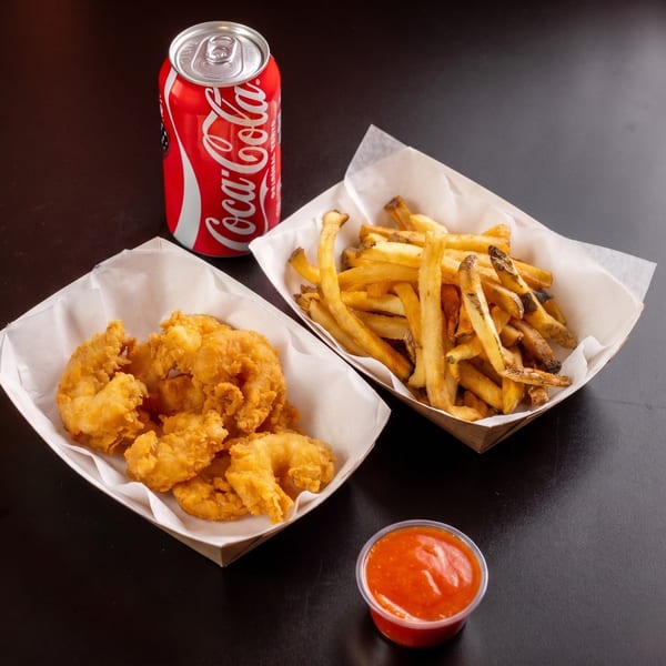 Fried shrimp, french fries, a Coca-Cola can, and a cup of red dipping sauce on a dark surface.