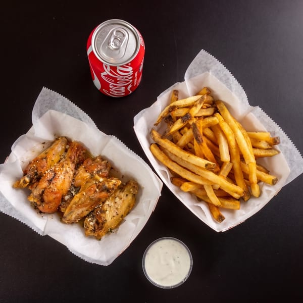 Garlic parmesan wings, french fries, a Coca-Cola can, and ranch dressing on a black surface.