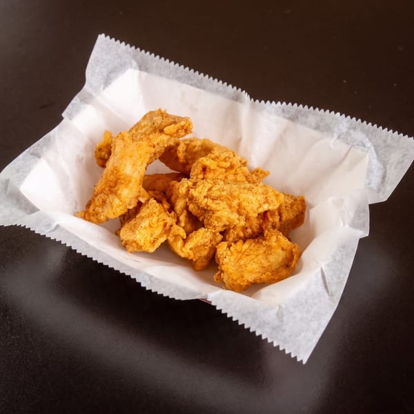 Crispy, golden-brown fried chicken tenders in a white paper-lined basket on a dark surface.