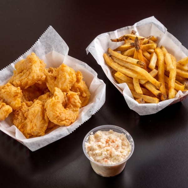 Fried shrimp and french fries in paper-lined baskets, with a side of coleslaw on a dark surface.