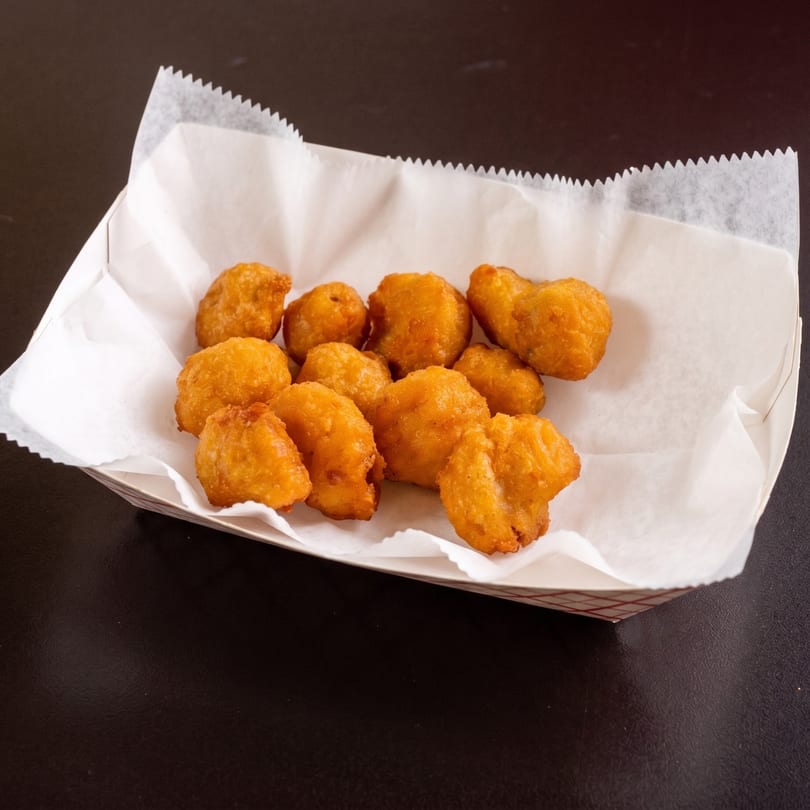 Golden-brown fried chicken nuggets in a white paper-lined basket on a dark surface.