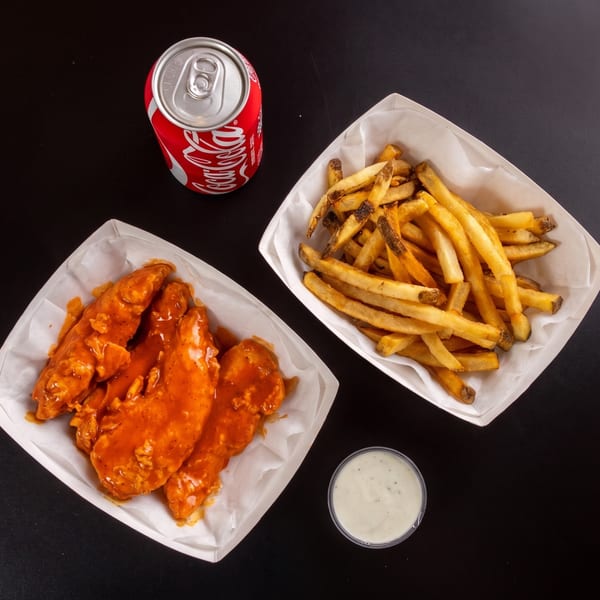 Top-down view of buffalo chicken tenders, fries, a Coca-Cola can, and ranch dressing on a black surface.